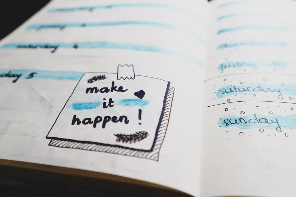 A planner page with "make it happen!" written on a sticky note, surrounded by days of the week and blue highlights.