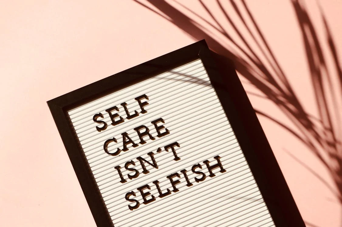 A letterboard sign with the message "SELF CARE ISN'T SELFISH" against a pink background with plant shadows.